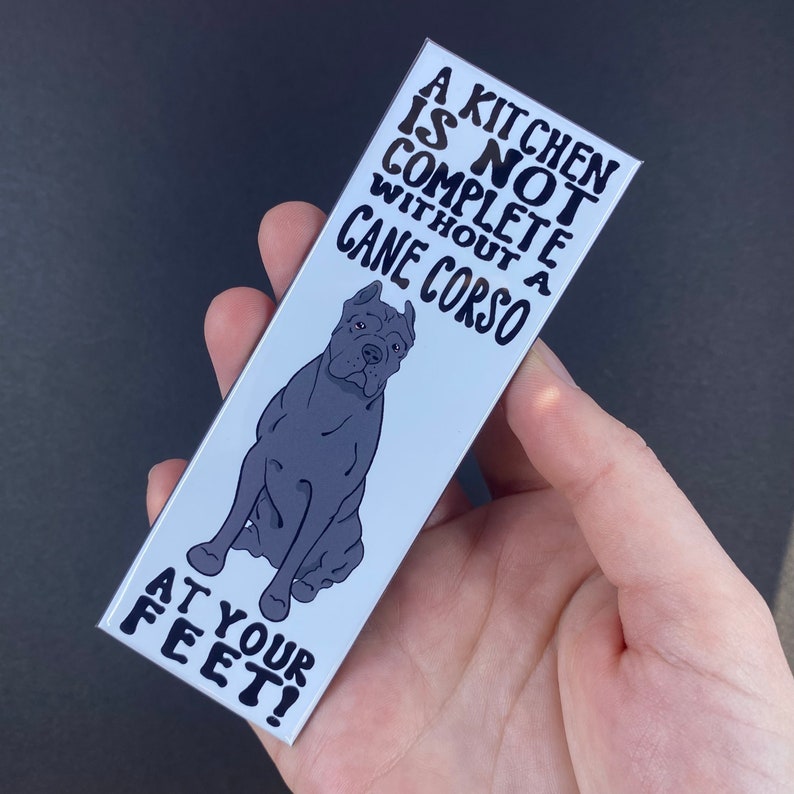 May include: A white bookmark with black text that reads "A kitchen is not complete without a Cane Corso at your feet!" and a black and white illustration of a Cane Corso.