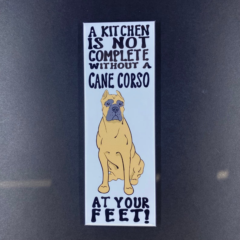 May include: A white magnet with black text that reads "A kitchen is not complete without a Cane Corso at your feet!" and a cartoon image of a tan Cane Corso dog sitting.