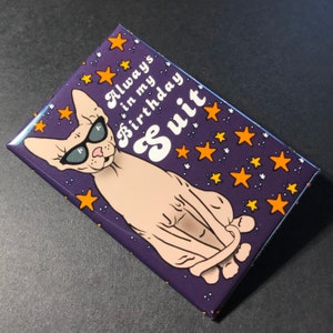 Puede incluir: Un im&aacute;n morado con un gato Sphynx de dibujos animados que lleva gafas de sol. El gato est&aacute; sentado con la cola enroscada alrededor de su cuerpo. El texto en el im&aacute;n dice "Always in my birthday suit".