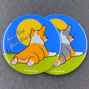 May include: Two round coasters featuring a cartoon image of a corgi dog with the text "Sun's Out Buns Out!" and "The Cloudy Corgi" on each coaster.