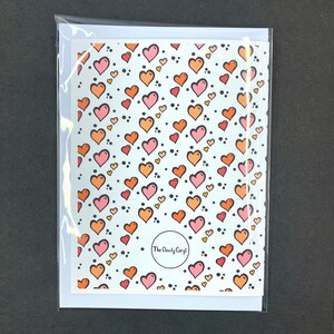 May include: A white card with a repeating pattern of pink and orange hearts on a light blue background. The card has the text "The Cloudy Corgi" in a circle at the bottom.
