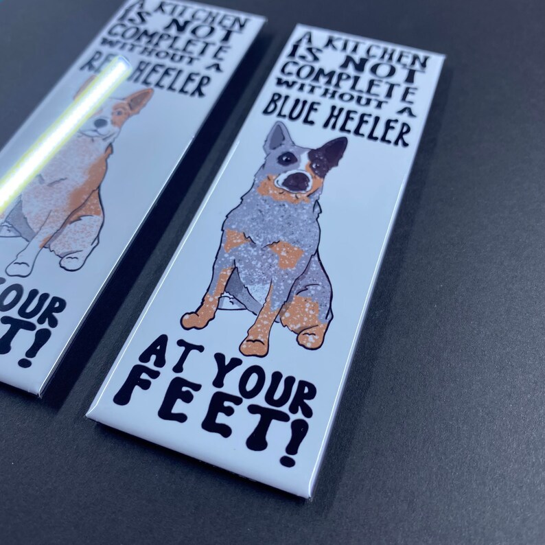 May include: Two white rectangular signs with a blue heeler dog illustration and the text "A kitchen is not complete without a blue heeler at your feet!"