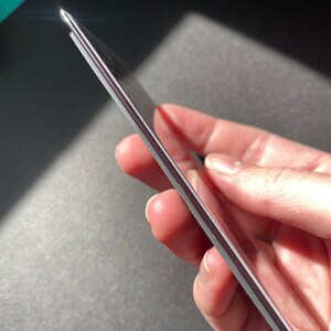 May include: A close-up of a silver phone case with a slightly textured surface. The case is held in a hand, showcasing its slim profile.