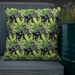 May include: Square throw pillow with a repeating pattern of green cannabis leaves on a black background with white polka dots. The pillow is resting on a gray surface.