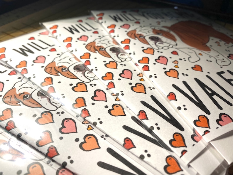 May include: A stack of Valentine's Day cards featuring a cartoon bulldog with hearts and the text "Will you be my Valentine?"