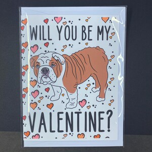 May include: A Valentine's Day card featuring a cartoon bulldog with the text "Will you be my Valentine?" surrounded by pink and orange hearts.