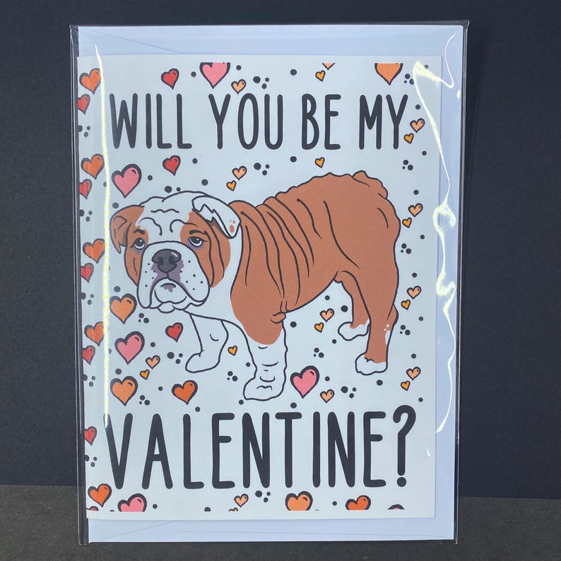 May include: A Valentine's Day card featuring a cartoon bulldog with the text "Will you be my Valentine?" surrounded by pink and orange hearts.