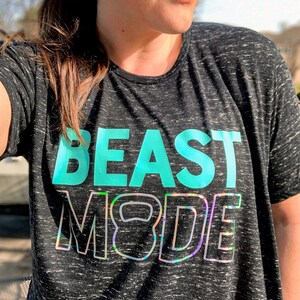 May include: A black and grey heather t-shirt with the text "BEAST MODE" in teal and iridescent lettering. The text includes a stylised kettlebell graphic.