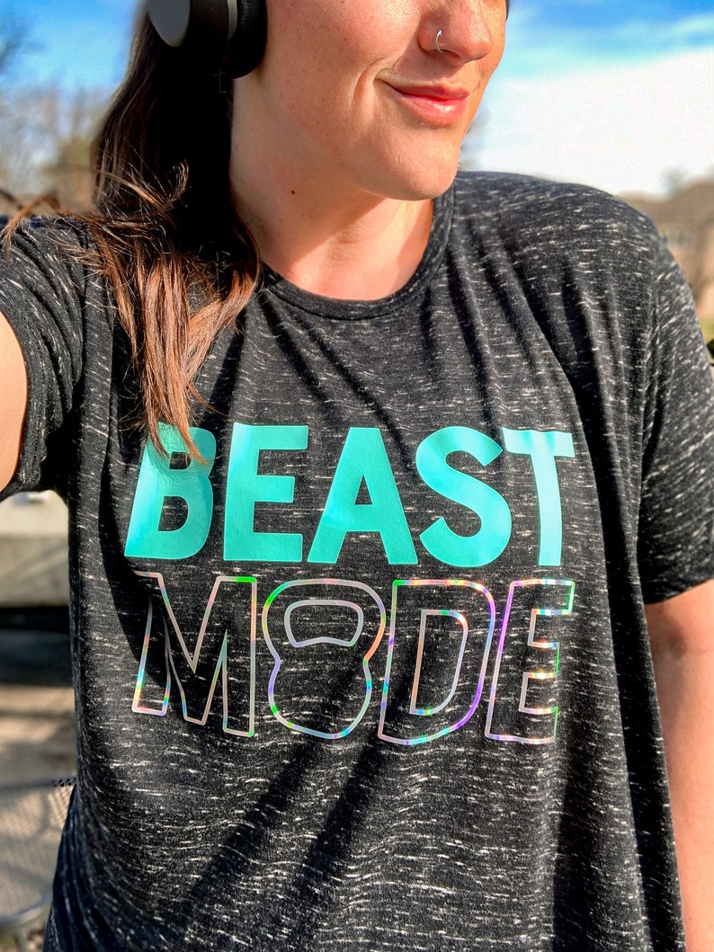 May include: A black and grey heather t-shirt with the text "BEAST MODE" in teal and iridescent lettering. The text includes a stylised kettlebell graphic.