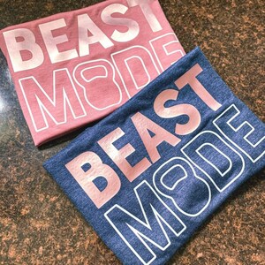 May include: Two t-shirts with the text "BEAST MODE" in rose gold lettering. The shirts are in different colours, one is pink and the other is blue.