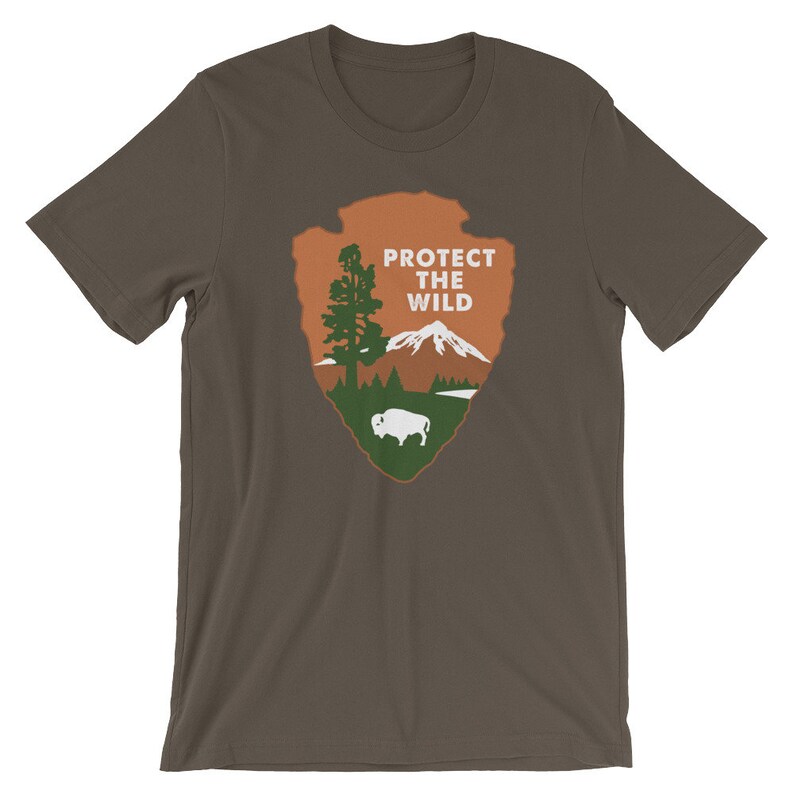 May include: A brown t-shirt with a brown, green, and white graphic of a mountain, a tree, and a buffalo. The graphic is in the shape of an arrowhead and says "Protect the Wild".