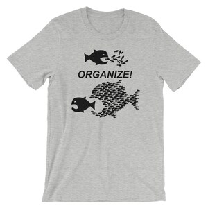 May include: A gray t-shirt with a black graphic of two fish. The top fish is eating smaller fish, and the bottom fish is made up of smaller fish. The text "ORGANIZE!" is printed on the shirt.
