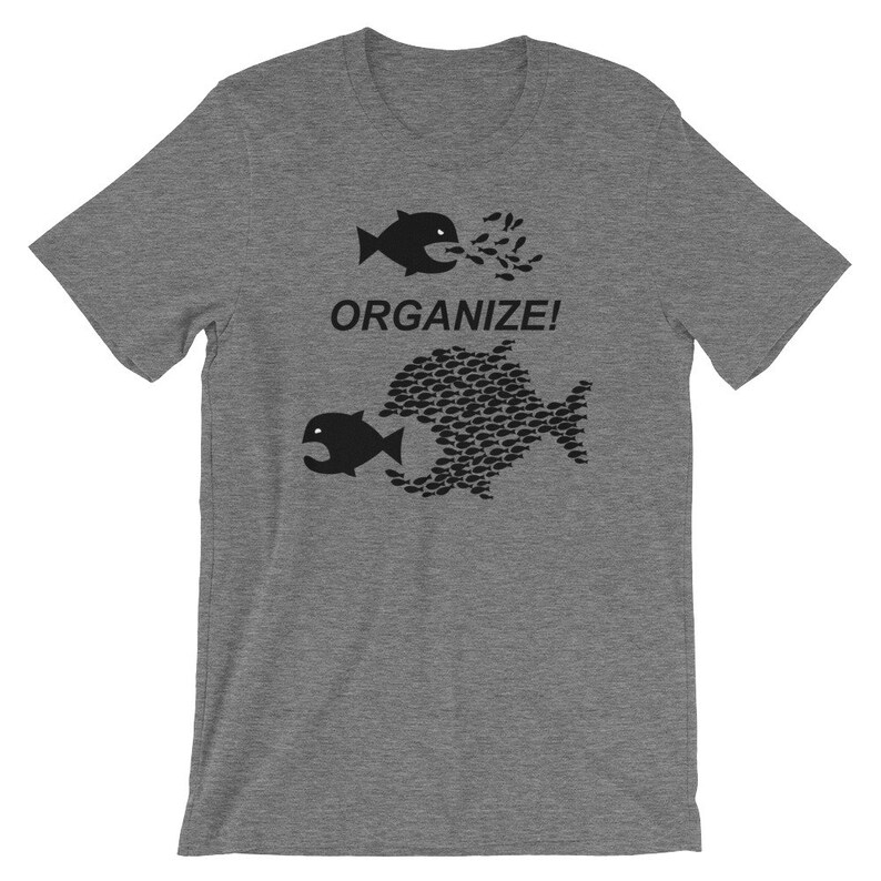 May include: A heather grey t-shirt with a black graphic of two fish. The smaller fish is being swallowed by the larger fish, which is made up of many smaller fish. The text "ORGANIZE!" is printed below the graphic.