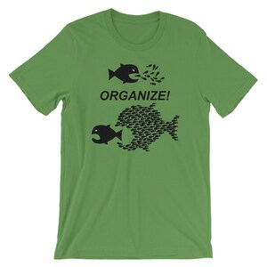 May include: A green t-shirt with a black graphic of two fish. The smaller fish is being swallowed by the larger fish, which is made up of many smaller fish. The text "ORGANIZE!" is printed above the fish.