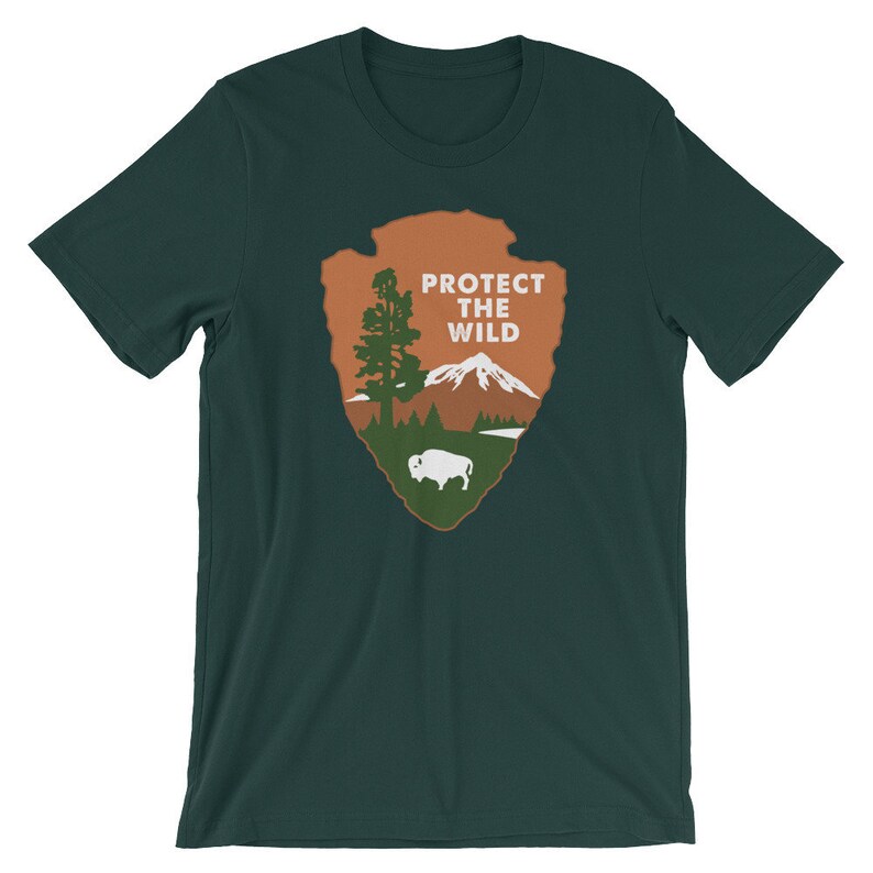 May include: A dark green t-shirt with a brown and green National Park Service inspired logo. The logo features a mountain, a tree, a buffalo, and the text "Protect the Wild".