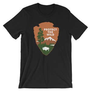 May include: Black t-shirt with a brown and green graphic of a mountain, tree, and buffalo. The graphic is in the shape of a teardrop and has the text "PROTECT THE WILD" in white.
