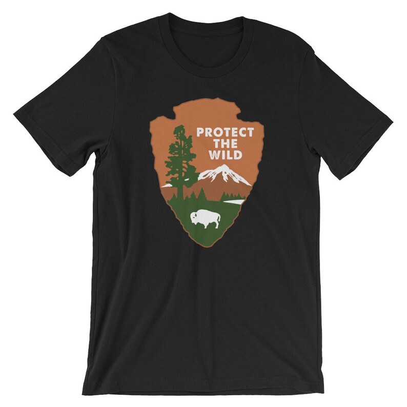 May include: Black t-shirt with a brown and green graphic of a mountain, tree, and buffalo. The graphic is in the shape of a teardrop and has the text "PROTECT THE WILD" in white.