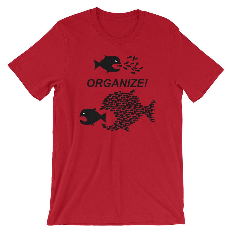 May include: Red t-shirt with a black graphic of two fish. The smaller fish is being swallowed by the larger fish, which is made up of many smaller fish. The text "ORGANIZE!" is printed below the fish.