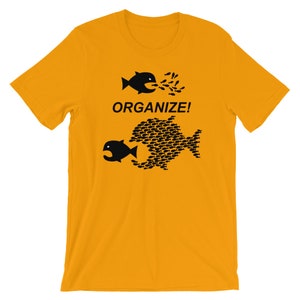 May include: A yellow t-shirt with a black graphic of two fish. The larger fish is made up of many smaller fish. The text "ORGANIZE!" is printed below the fish.