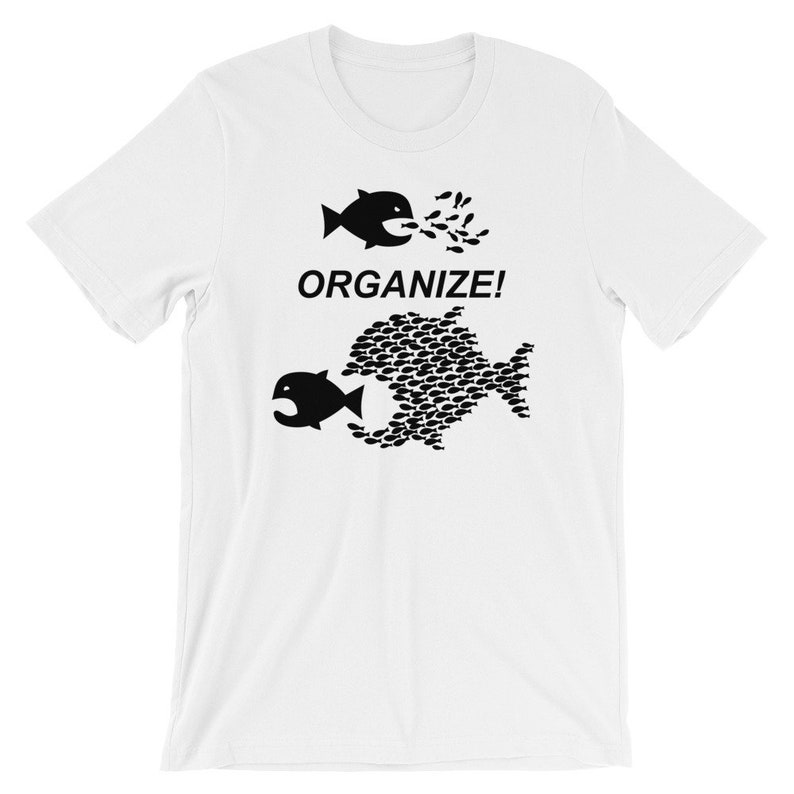 May include: White t-shirt with a black graphic of two fish. The top fish is small and being eaten by a larger fish made up of many smaller fish. The text "ORGANIZE!" is printed below the fish.