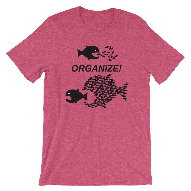 May include: A pink t-shirt with a black graphic of two fish. The smaller fish is being swallowed by the larger fish, which is made up of many smaller fish. The text "ORGANIZE!" is printed above the fish.