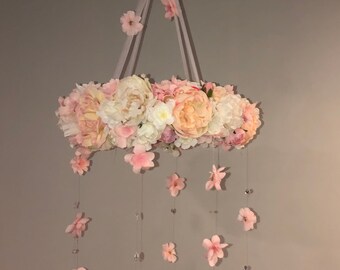 May include: A pink and white floral mobile with a circular base of flowers and pink flowers hanging from the base.