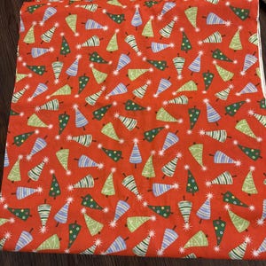Puede incluir: Tela roja con un patrón repetido de árboles de Navidad estilizados en verde, azul y blanco. Los árboles tienen detalles de estrellas y están dispersos por la tela.