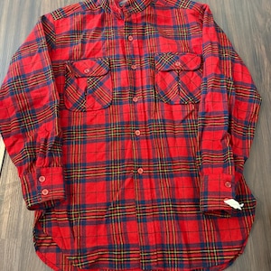 May include: A long-sleeved button-down shirt featuring a vibrant red, navy blue, and yellow plaid pattern. The shirt includes a stand-up collar, two chest pockets with buttoned flaps, and buttoned cuffs. The fabric has a soft, brushed texture.