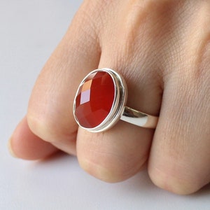 May include: A silver ring with a red carnelian gemstone. The ring has a bezel setting and a smooth, polished finish.