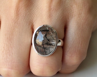May include: A silver ring with a clear oval-shaped stone with black inclusions. The stone is set in a silver bezel.