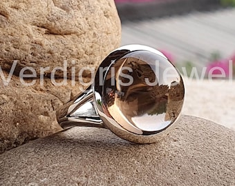 May include: A silver ring with a round, clear, smoky quartz gemstone. The ring is sitting on a brown rock.