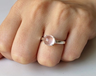 Puede incluir: Un anillo de plata con una piedra redonda de color rosa pálido. El anillo está en un dedo.