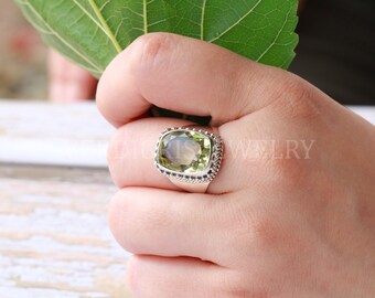 May include: A silver ring with a large, light green gemstone set in a bezel setting. The ring has a beaded edge.