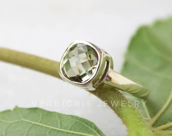 May include: A silver ring with a light green square-shaped gemstone. The ring is sitting on a green leaf.