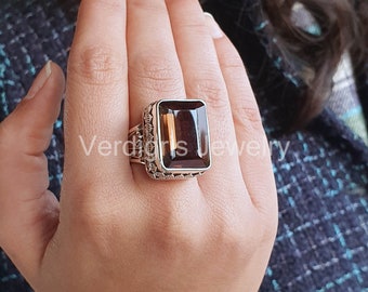 May include: A silver ring with a large, rectangular, smoky quartz gemstone. The ring has an intricate, detailed design around the stone.