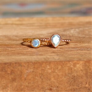 May include: Two gold rings with iridescent gemstone settings. The ring on the left has a round stone, while the ring on the right has a teardrop-shaped stone.