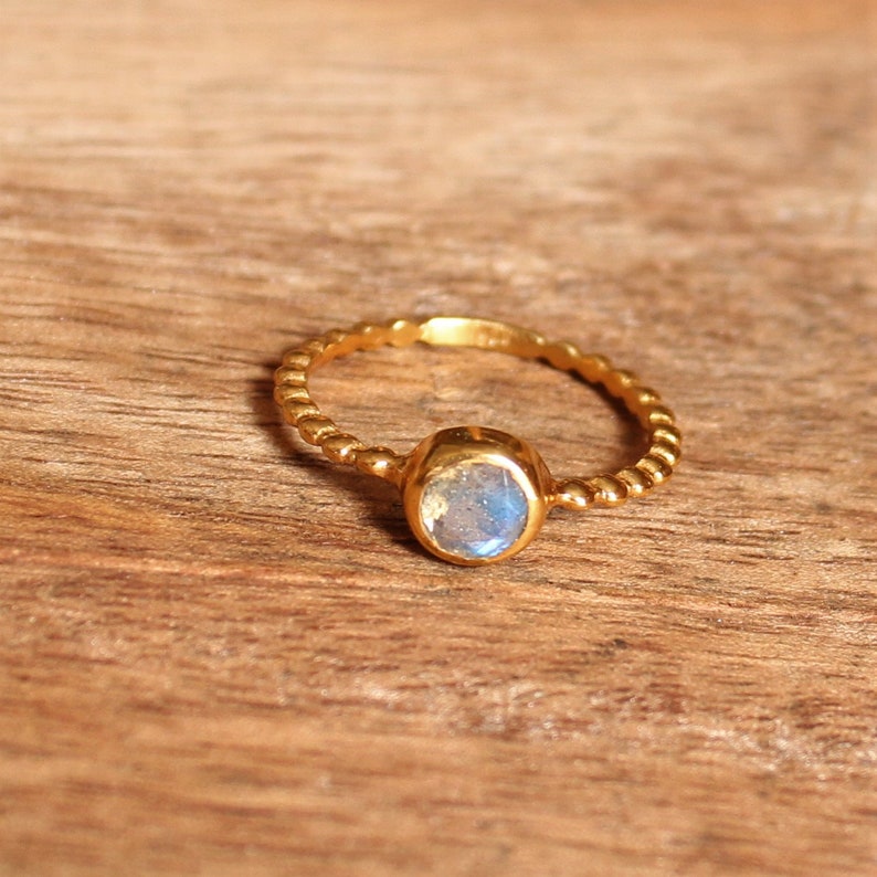 May include: A gold ring with a light blue oval gemstone. The ring band is twisted and has a beaded design.