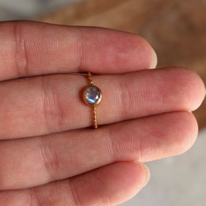 May include: A delicate gold ring with a round iridescent moonstone gemstone.