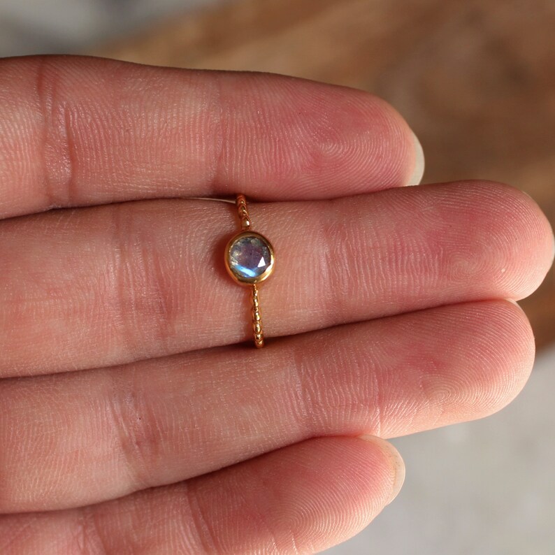 May include: A delicate gold ring with a round iridescent moonstone gemstone.