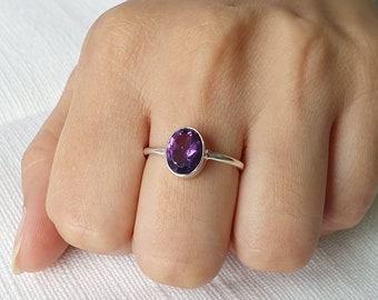 May include: A silver ring with a round, purple amethyst gemstone.