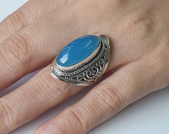 May include: A silver ring with an oval-shaped blue gemstone set in a detailed silver band.