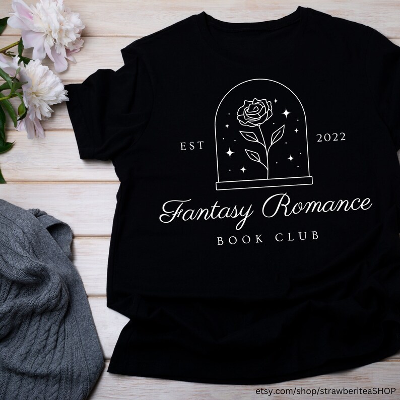 K&ouml;nnte beinhalten: Schwarzes T-Shirt mit einem wei&szlig;en Grafikdesign einer Rose in einer Glaskuppel mit Sternen. Der Text "Fantasy Romance Book Club" befindet sich unter der Kuppel. Der Text "Est 2022" befindet sich auf beiden Seiten der Kuppel.