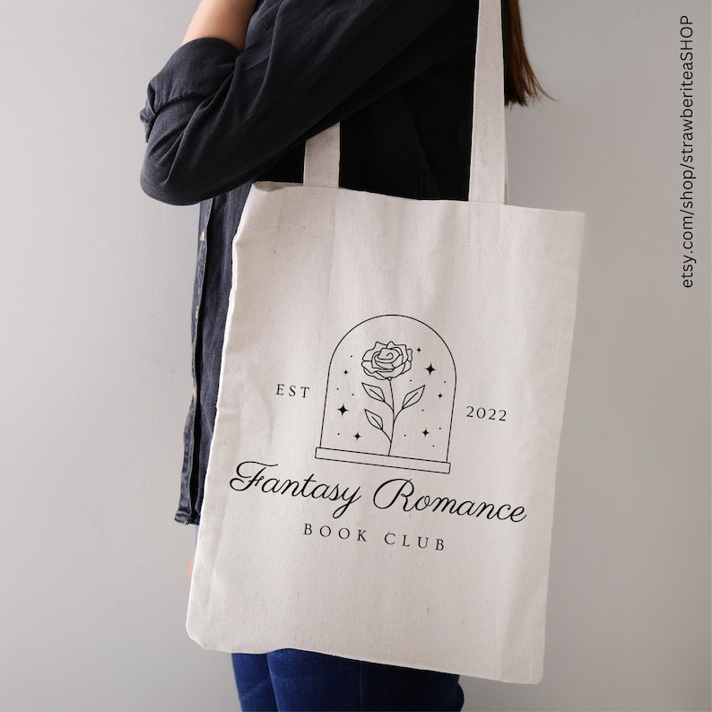 K&ouml;nnte beinhalten: Wei&szlig;e Stofftasche mit einem schwarzen grafischen Design, das eine Rose in einer Glaskuppel mit Sternen zeigt. Der Text "EST 2022 Fantasy Romance Book Club" ist unter dem Grafikdruck.