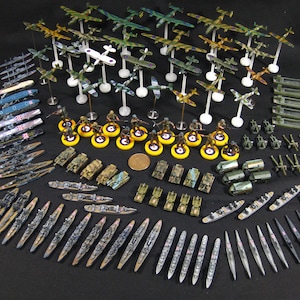 Peut inclure: Une collection de figurines de jeux de guerre miniatures, comprenant des avions, des navires, des chars et des soldats. Les modèles sont peints de différentes couleurs, avec des motifs détaillés. Les pièces sont disposées sur une surface sombre, suggérant un jeu de table.