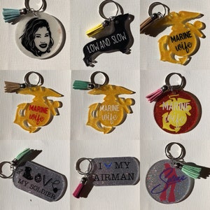 May include: Nine different keychains with various designs and colors. Some keychains feature glitter, while others have a smooth finish. The keychains feature text such as "Marine wife", "Low and Slow", "Love My Soldier", and "I My Airman".