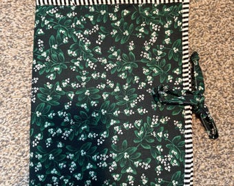 Puede incluir: Un artículo de tela verde oscuro con un estampado floral blanco y un borde a rayas blanco y negro. Una corbata de tela a juego está unida al costado. El artículo es probablemente una cubierta de diario o cuaderno.