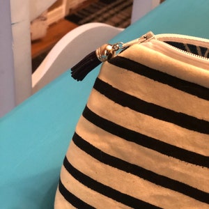 Puede incluir: Una bolsa con cremallera a rayas blancas y negras con un borla negra. La bolsa est&aacute; hecha de tela y tiene una cremallera blanca.