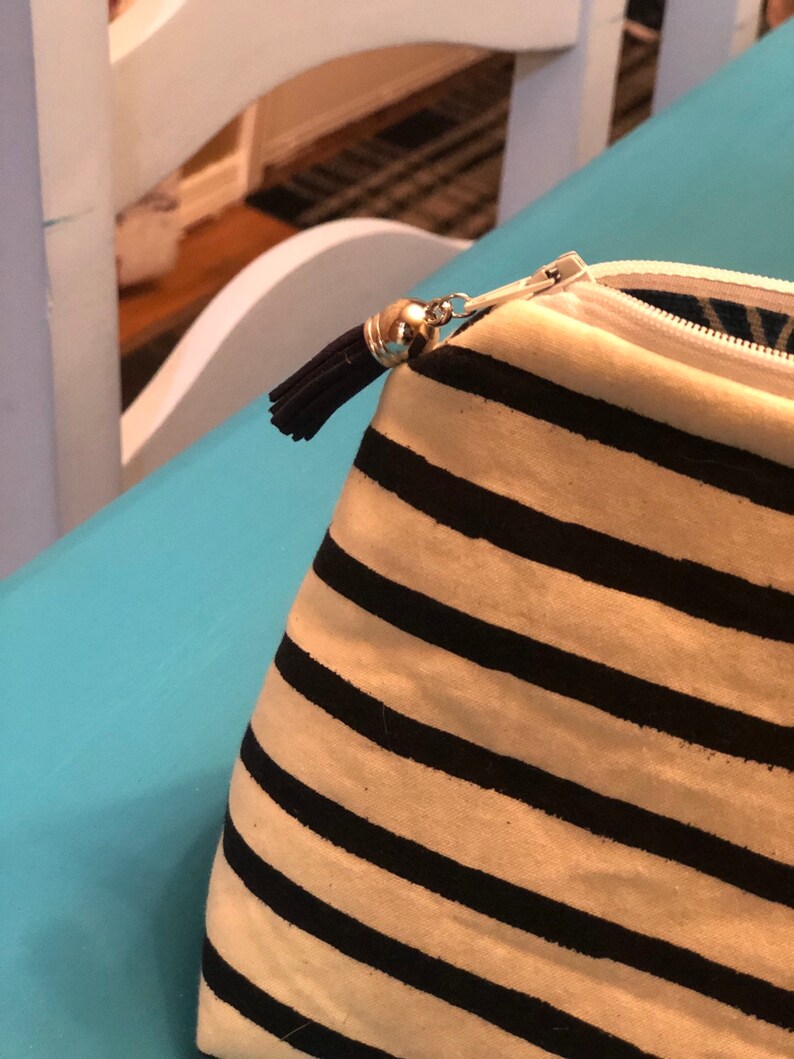 Puede incluir: Una bolsa con cremallera a rayas blancas y negras con un borla negra. La bolsa est&aacute; hecha de tela y tiene una cremallera blanca.