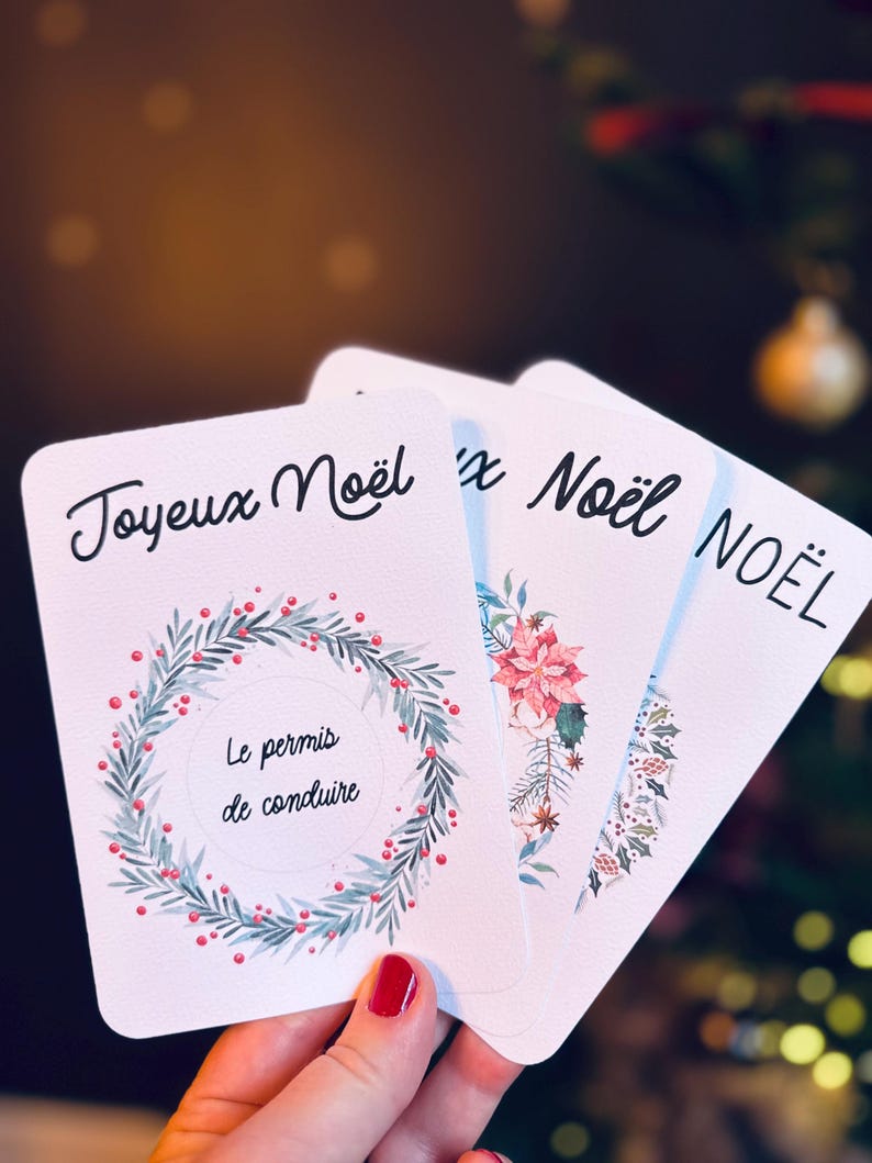 May include: Four white cards with Christmas greetings in French. The top card has a wreath with red berries and green leaves and the text 'Joyeux Noël' and 'Le permis de conduire'. The second card has a pink flower and the text 'x Noël'. The third card has a green and red floral design and the text 'NOËL'.
