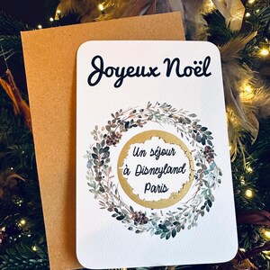 May include: A white card with a gold wreath and the words 'Joyeux Noël' and 'Un séjour à Disneyland Paris'.